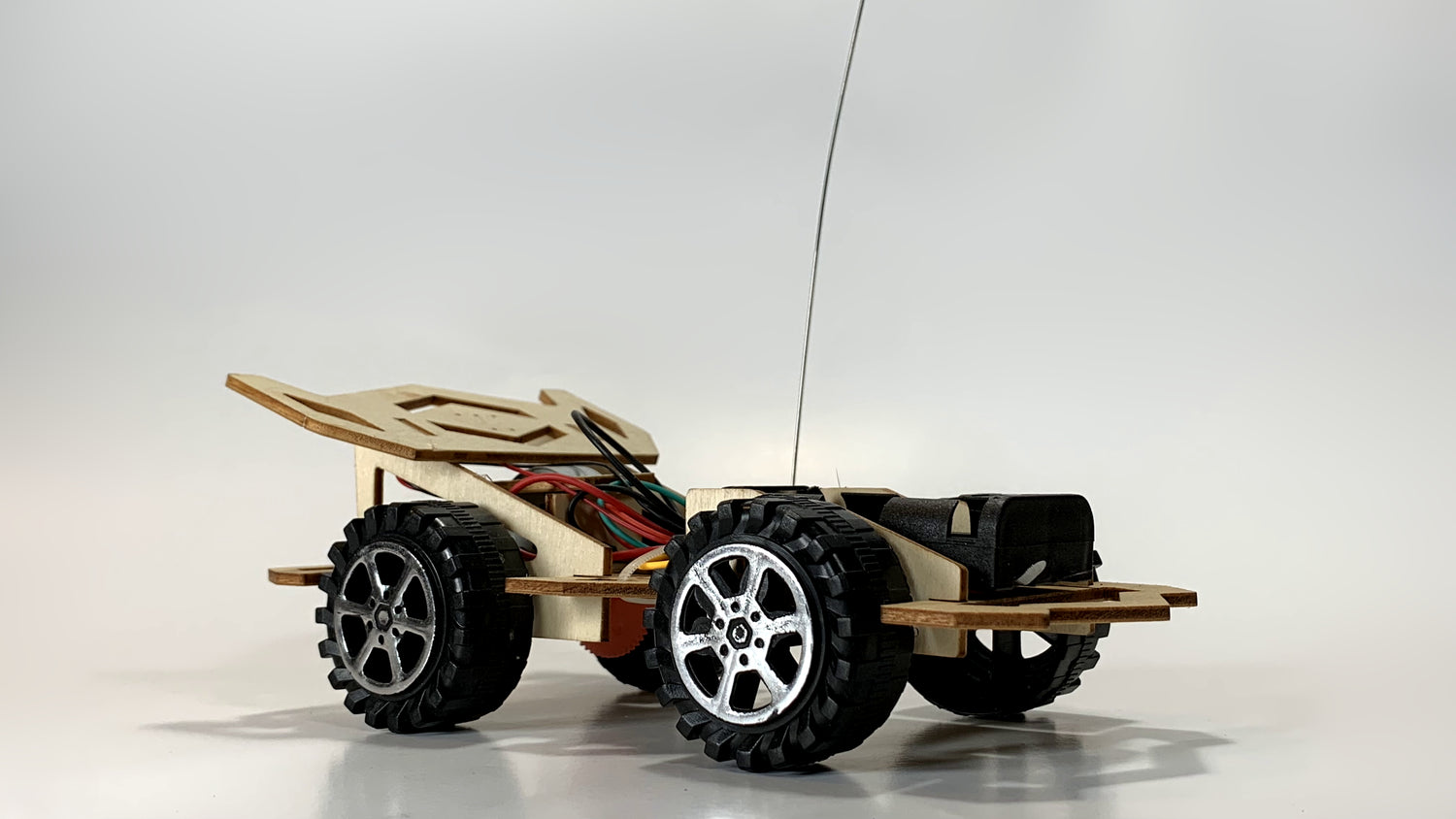 Angled rear view of the remote control Race Car STEM Kit, featuring rugged black wheels, exposed wiring, and a wooden body structure