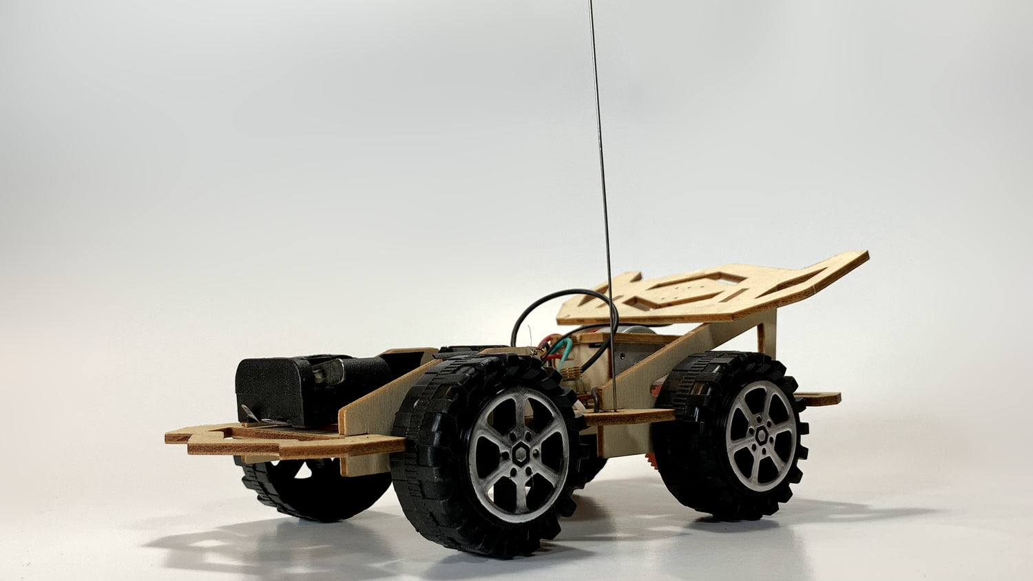 Rear angle view of the Remote Control Race Car STEM Kit showing wooden chassis, rugged wheels, antenna, and exposed wiring for electronics assembly