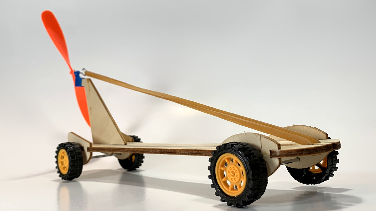 Rear angled view of the Rubber Band Race Car STEM Kit showcasing a wooden structure, bright orange propeller, stretched rubber band, and durable yellow wheels